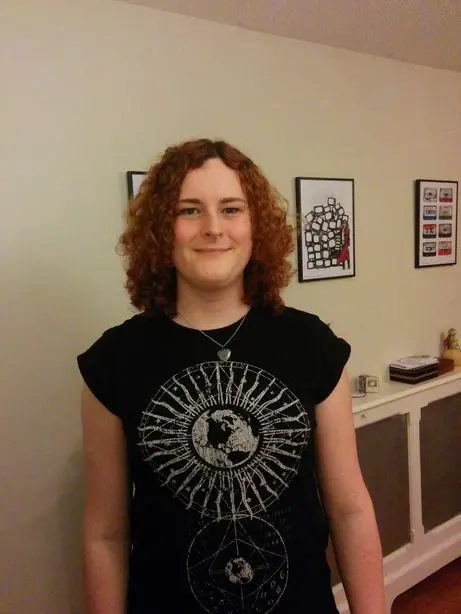A somewhat tall girl with a black t-shirt on with long curly red-brown hair